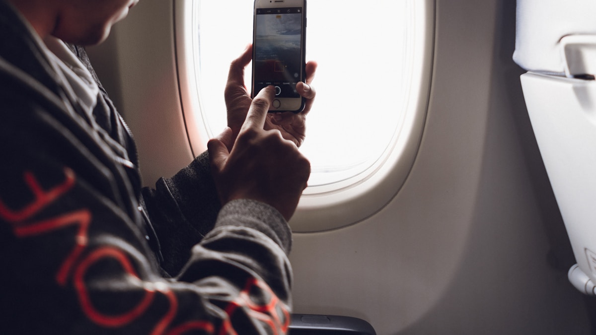 Traveler using a smartphone next to an airplane window comparing wireless plans
