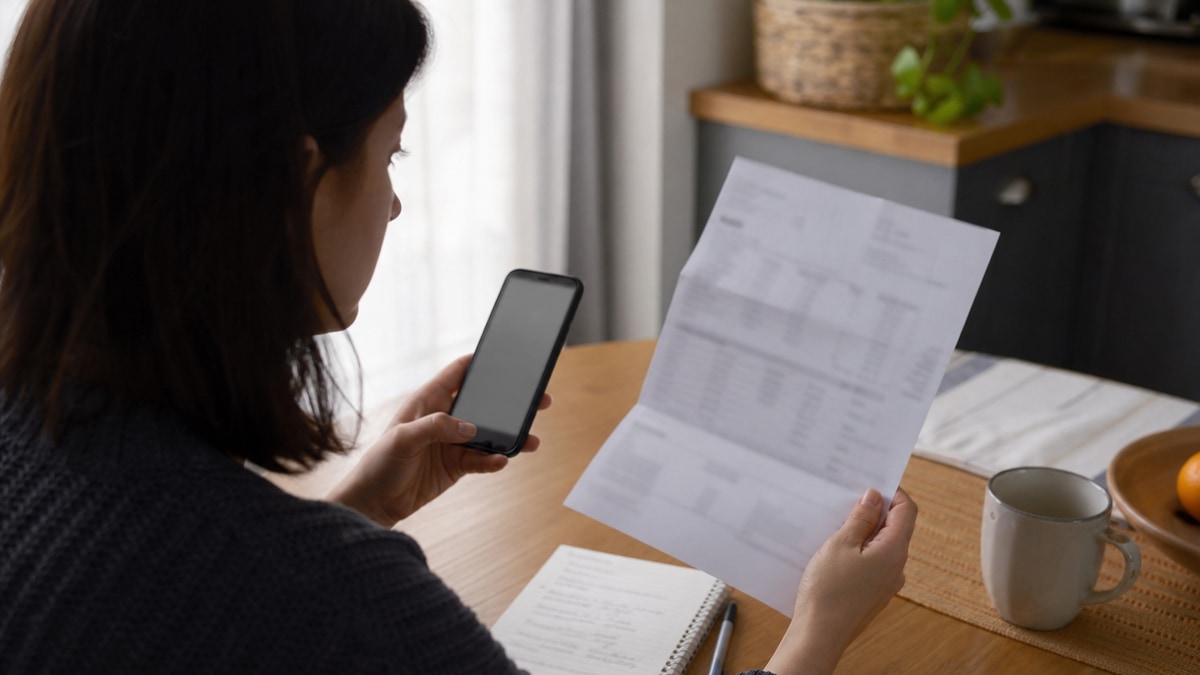 A shopper reviews a blurred phone bill and smartphone at a kitchen table before switching wireless plans